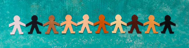 Banner of a multi-ethnic paper dolls chain holding hands against racism A group of paper dolls in a row colored as the different human skins line of people holding hands stock pictures, royalty-free photos & images