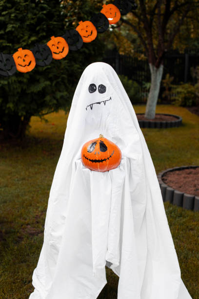 istock Ghost holds pumpkin with spooky face in green backyard 1336263638