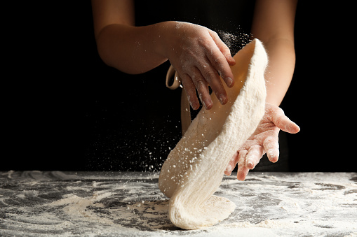 Woman kneading dough for pizza at grey table, closeup