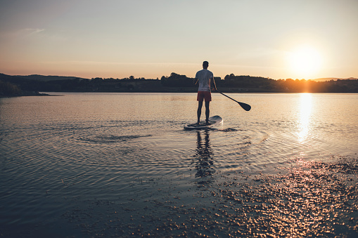 Photo of a man floating on the lake on his paddle board at sunset.