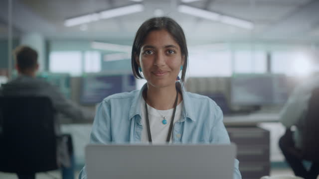 Diverse Office: Portrait of Beautiful Indian IT Programmer Working on Desktop Computer, Smiling and Looking at Camera Kindly. Female Software Engineer Creating Innovative App, Program, Video Game