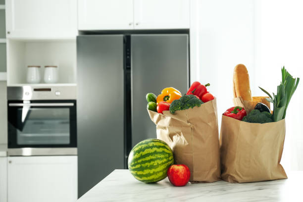 istock Paper bags with fresh products on table near modern refrigerator in kitchen 1336265294