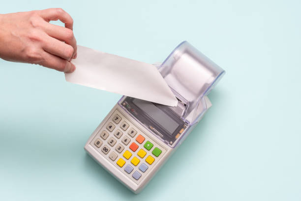 Close-up of a hand holding a blank white check on a cash register against a blue background, receipt, retail.