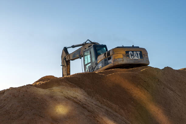 Yellow excavator 3/4 back view digging at the top of a pile of sand. stock photo