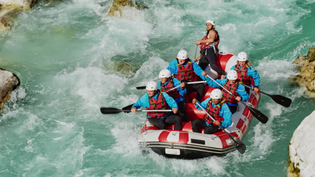 Rafting team navigating the rapids around a large rock