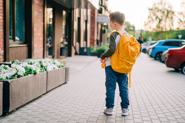 学校に戻る。学校に行くバックパックを持つかわいい子供。バッグを持つ少年の生徒。授業に行く小学生。クラスの後、街の通りを屋外で歩く子供。バックビュー - elementary school building ストックフォトと画像