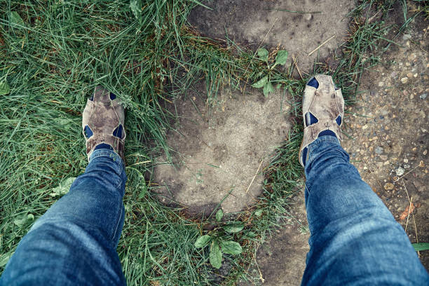 istock Legs in jeans and old brown sandals on old road with grass 1336271685