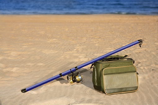 Fishing surfcasting rod and box over beach sand sea background