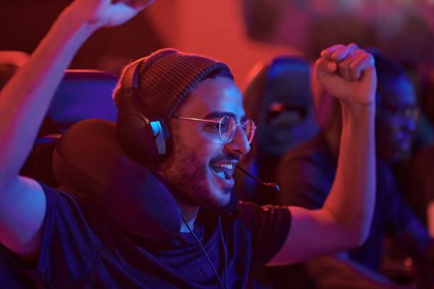 istock Cheerful young mixed race man in headset with microphone making yes gesture while celebrating winning in game 1336273210