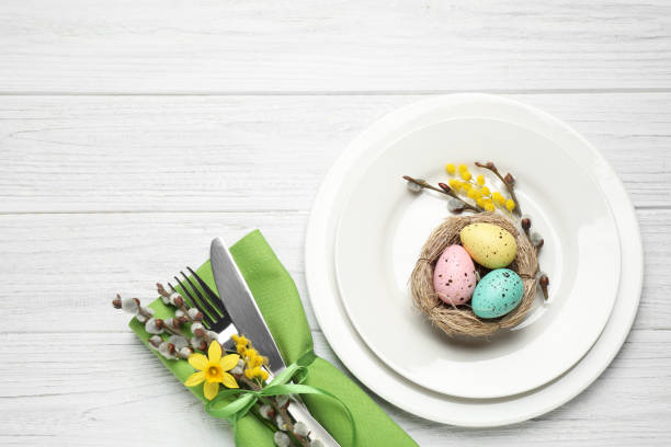 istock Festive Easter table setting with quail eggs and floral decor on white wooden background, flat lay 1336273604