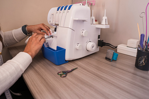 Average 45-year-old Latina woman dressed casually as a fashion designer stands in her sewing workshop preparing her sewing machine