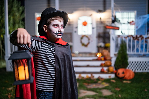 Boy in vampire costume holding lantern and having fun on Halloween trick or treat