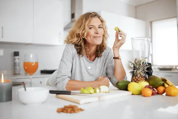 Photo of Shot of a woman preparing and eating fruit before making a smoothie
