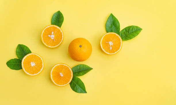 istock Oranges are laid out with leaves on a yellow background 1336278924