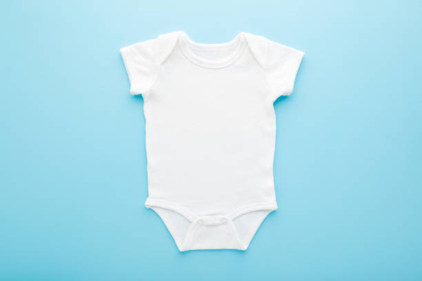 nuevo bodysuit de bebé blanco sobre fondo de mesa azul claro. color pastel. closeup. lugar vacío para el texto o el logotipo en la ropa. vista de arriba hacia abajo. - onesie fotografías e imágenes de stock