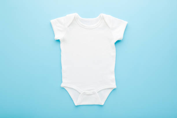 White new baby bodysuit on light blue table background. Pastel color. Closeup. Empty place for text or logo on apparel. Top down view. White new baby bodysuit on light blue table background. Pastel color. Closeup. Empty place for text or logo on apparel. Top down view. babygro stock pictures, royalty-free photos & images