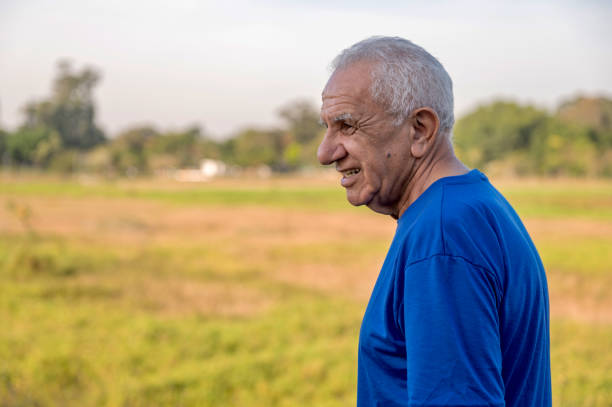 side portrait of a senior man wearing blue t-shirt walking alone at a park on a sunny day
