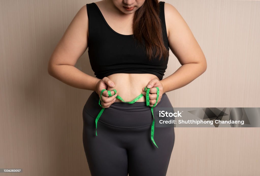 beautiful fat woman in sportswear catches her big belly or belly fat with tape measure. healthy weight control concept. overweight, bloated belly Dieting Stock Photo