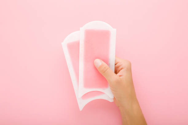 young adult woman hand holding two wax strips on light pink table background. pastel color. closeup. female product for smooth body skin. top down view. - waxing armpit women beauty treatment imagens e fotografias de stock