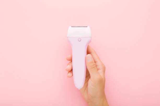 Young adult woman hand holding electric epilator on light pink table background. Pastel color. Closeup. Female product for smooth body skin. Top down view. Young adult woman hand holding electric epilator on light pink table background. Pastel color. Closeup. Female product for smooth body skin. Top down view. epilator stock pictures, royalty-free photos & images