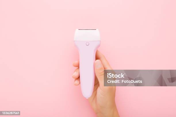 Young Adult Woman Hand Holding Electric Epilator On Light Pink Table Background Pastel Color Closeup Female Product For Smooth Body Skin Top Down View Stock Photo - Download Image Now