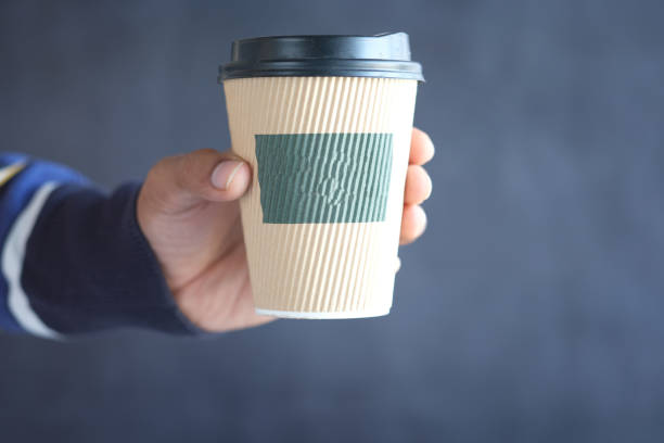 istock hand holding take away paper cup against black background. 1336288071