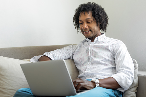 African American man sitting on couch and using laptop