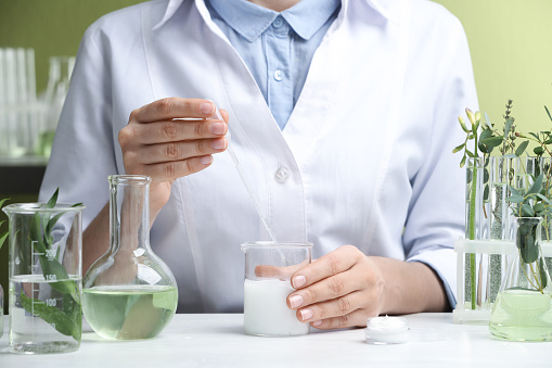 Woman working with cream at table in cosmetic laboratory, closeup