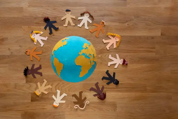 Multi-ethnic paper dolls with different colored hair holding hands and surrounding our beautiful planet