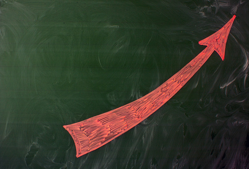 A large pink arrow pointing upwards is drawn on a green blackboard with traces of chalk and space for copying. Concept-success and career growth