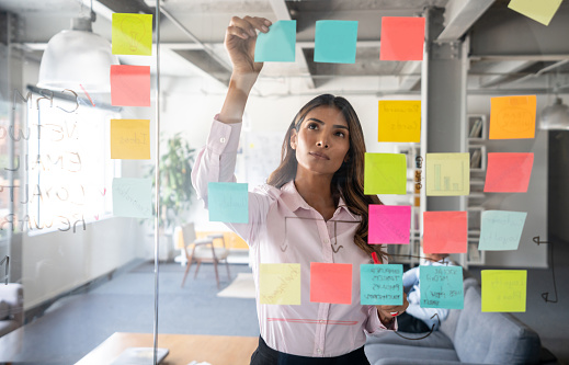 Latin American woman making a business plan at the office using adhesive notes on the board - productivity concepts