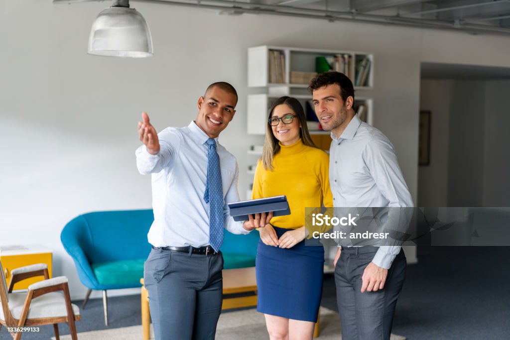 Real Estate Agent showing a property to a happy couple Latin American Real Estate Agent showing a property to a happy couple and pointing away - real estate concepts Real Estate Agent Stock Photo