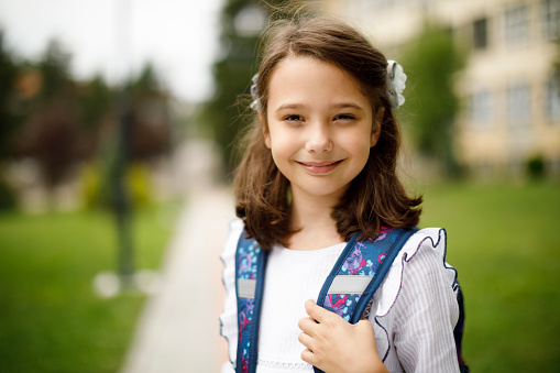 Portrait of cute smiling schoolgirl in front of the school
