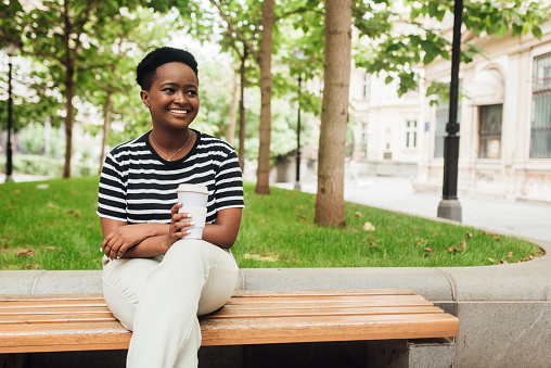 Portrait of an African American young woman sitting on the bench and enjoying coffee.