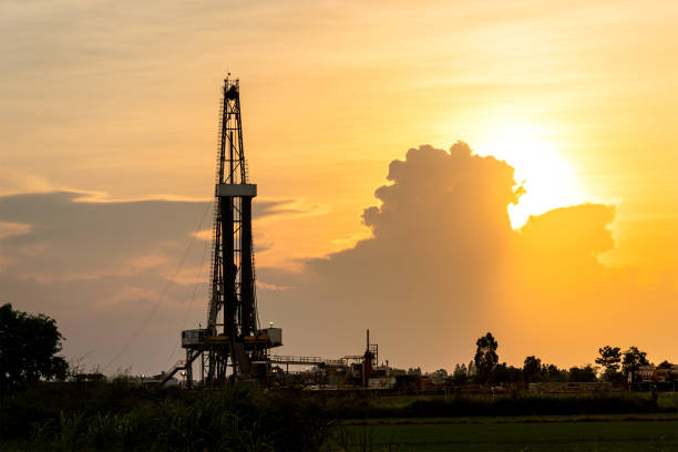 Silhouette black shadow of oil exploration drilling rig. Silhouette black shadow of oil exploration drilling rig structure among the orange sunrise sky and agriculture field environemnt. Energy industrial background photo. oil field stock pictures, royalty-free photos & images