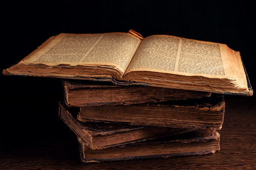 Stack of old worn shabby Jewish books in leather binding in the dark. Open page of Torah. Closeup. Selective focus. Low key
