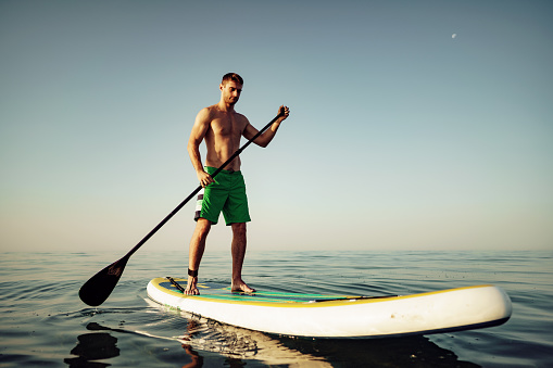 Young fit man on paddle board floating on lake at sunrise