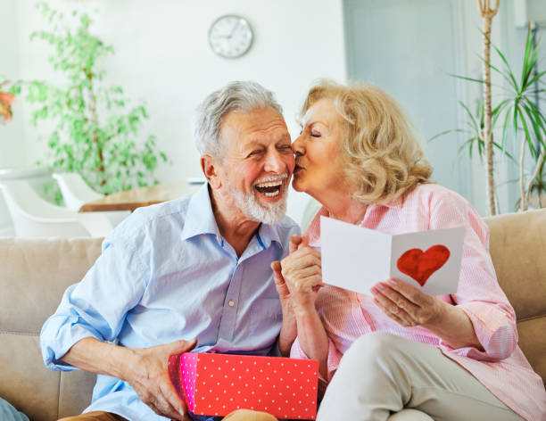 gift woman man couple happy love happiness present kiss romantic smiling together box wife husband elderly old senior mature retired Smiling senior woman receives present box and kissing her husband for giving her a present at home valentines day stock pictures, royalty-free photos & images