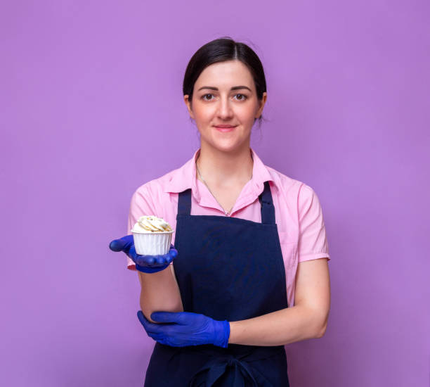Portrait of a pastry chef woman in an apron and gloves, holding a ready-made cupcake with her hand. Selective focus. stock photo