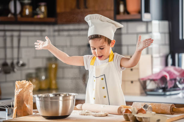 istock Toddler boy playing with the dough in the kitchen dressed as a chef. Child baking a cake 1336316780