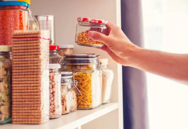 Photo of A Man Takes or Places Glass Jars Filled With Legumes From A Shelf In The Pantry