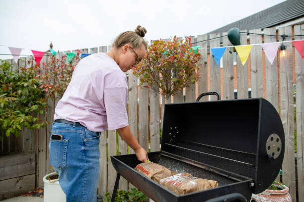 Lighting the BBQ Woman in her garden in the North East of England lighting up a BBQ. She is throwing a social gathering in summer. grill lighter stock pictures, royalty-free photos & images
