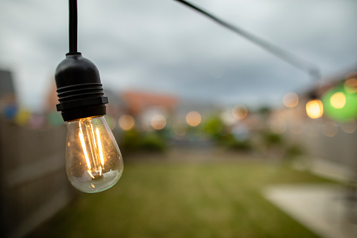 Close up of an illuminated light bulb hanging in a garden at dusk in the North East of England. There is copy space beside the bulb.