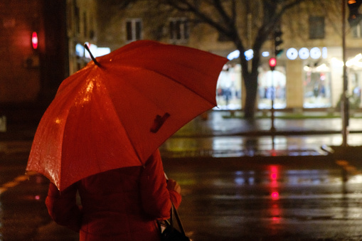 Rainy evening. A woman silhouette with umbrella and running traffic with drops of rain. Autumn time. Red umbrella
