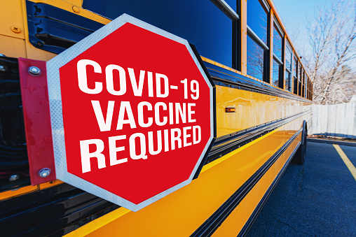 COVID-19 Vaccination Required overlaid on school bus stop sign.