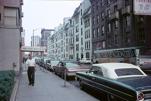 New York City, NY, USA, 1964. Street scene with pedestrians, parked cars and buildings on the 8th corner of 5th Avenue in Midtown Manhattan.