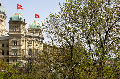 Bern, Switzerland - April 22, 2019: Large building of The Federal Palace, it is the seat of Federal Parliament (Swiss Federal Assembly). There are trees nearby. The City of Bern is one of the countless great places in Switzerland and it is the political centre of this Country. Numerous museums, a wide cultural offer, a variety of tourist attractions makes it a travel destination for tourists from all over the world.