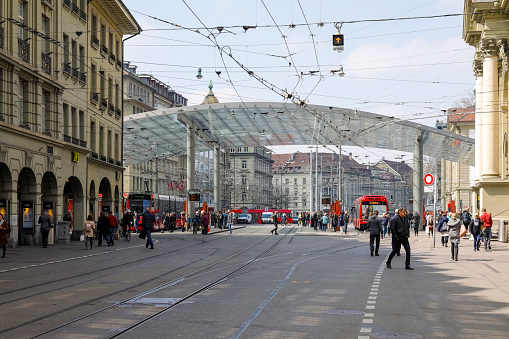 Bern, Switzerland - April 15, 2019: In between the buildings there is a modern public transport stop and it is covered by a large glass roof. At this public transport stop, people are waiting. The City of Bern is one of the countless great places in Switzerland and it is the political centre of this Country. Numerous museums, a wide cultural offer, a variety of tourist attractions makes it a travel destination for tourists from all over the world.