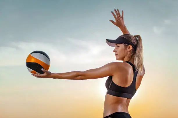 girl athlete volleyball player on the beach playing at sunset.