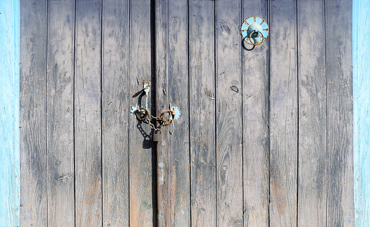 Old wooden gate closed with a padlock on a chain. Retro wood door with vintage metal decorative elements